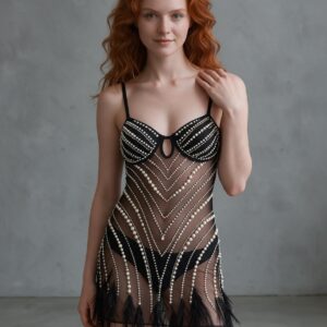 A woman in a black rhinestone sheer mini dress with a feather hem, one hand on her shoulder, gray concrete studio.