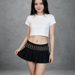 A woman in a black studded pleated mini skirt and a white crop top, holding the side of the skirt, gray concrete studio.